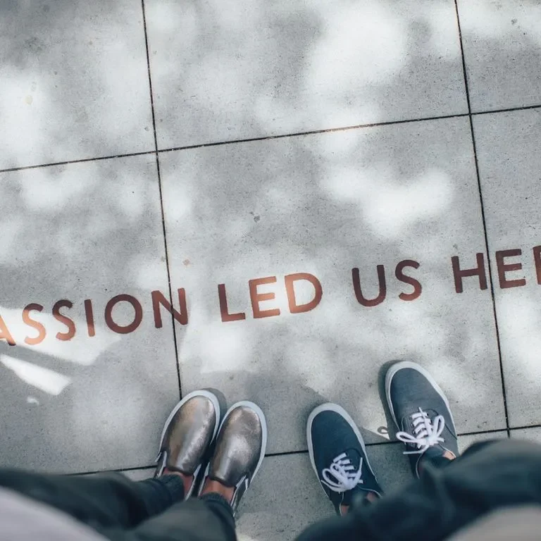 “Feet on a stone path with the text ‘Passion Led Us Here’ visible.”