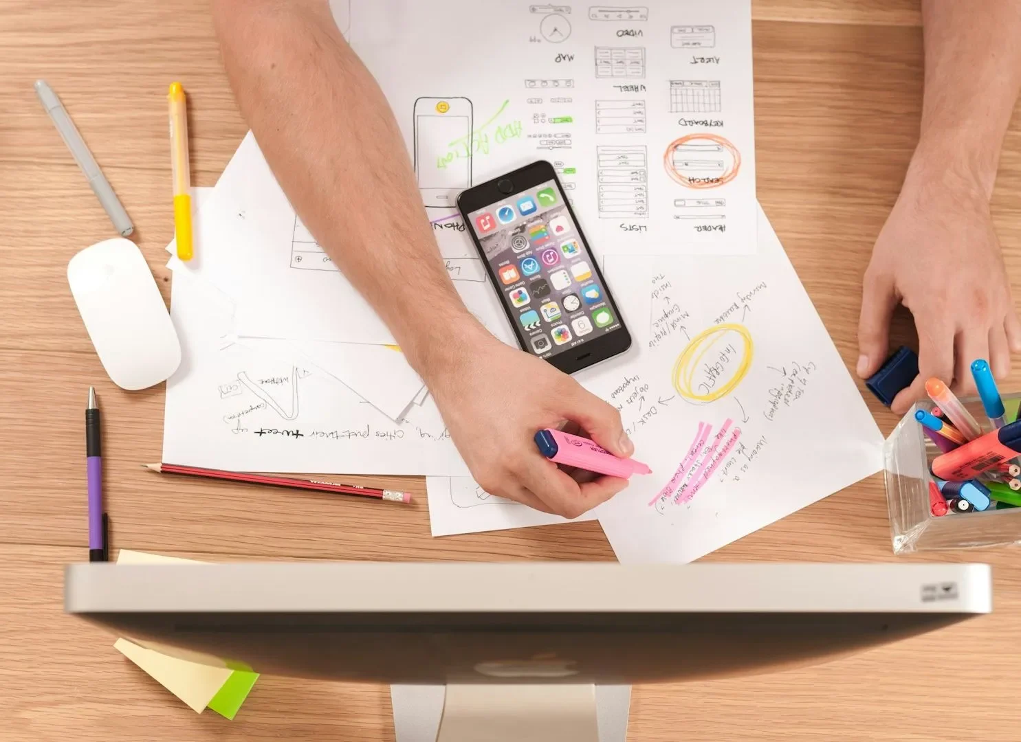 Person highlighting notes on app wireframe sketches with a smartphone on desk